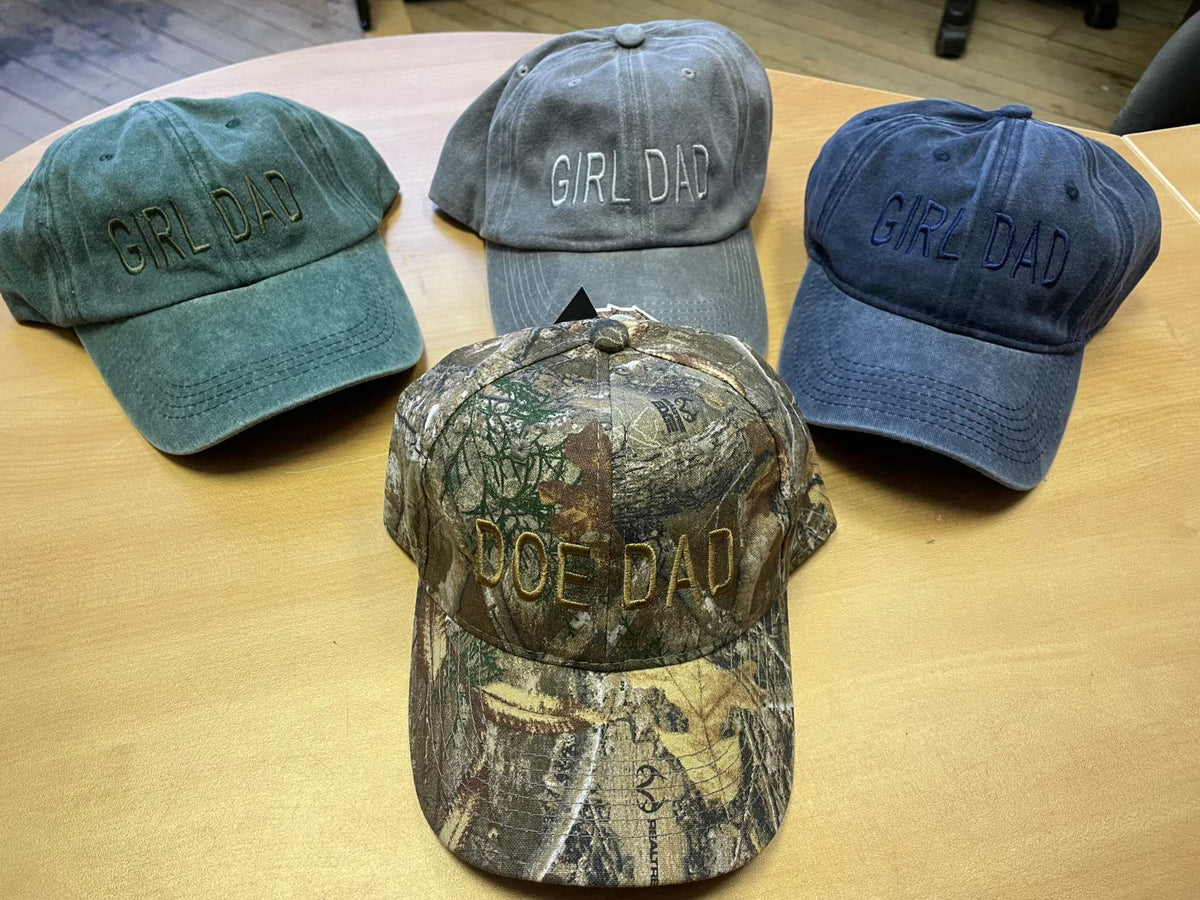 Cotton brushed adjustable baseball hats with "Girl Dad" and "Doe Dad" embroidery in green, gray, blue, and camo colors.