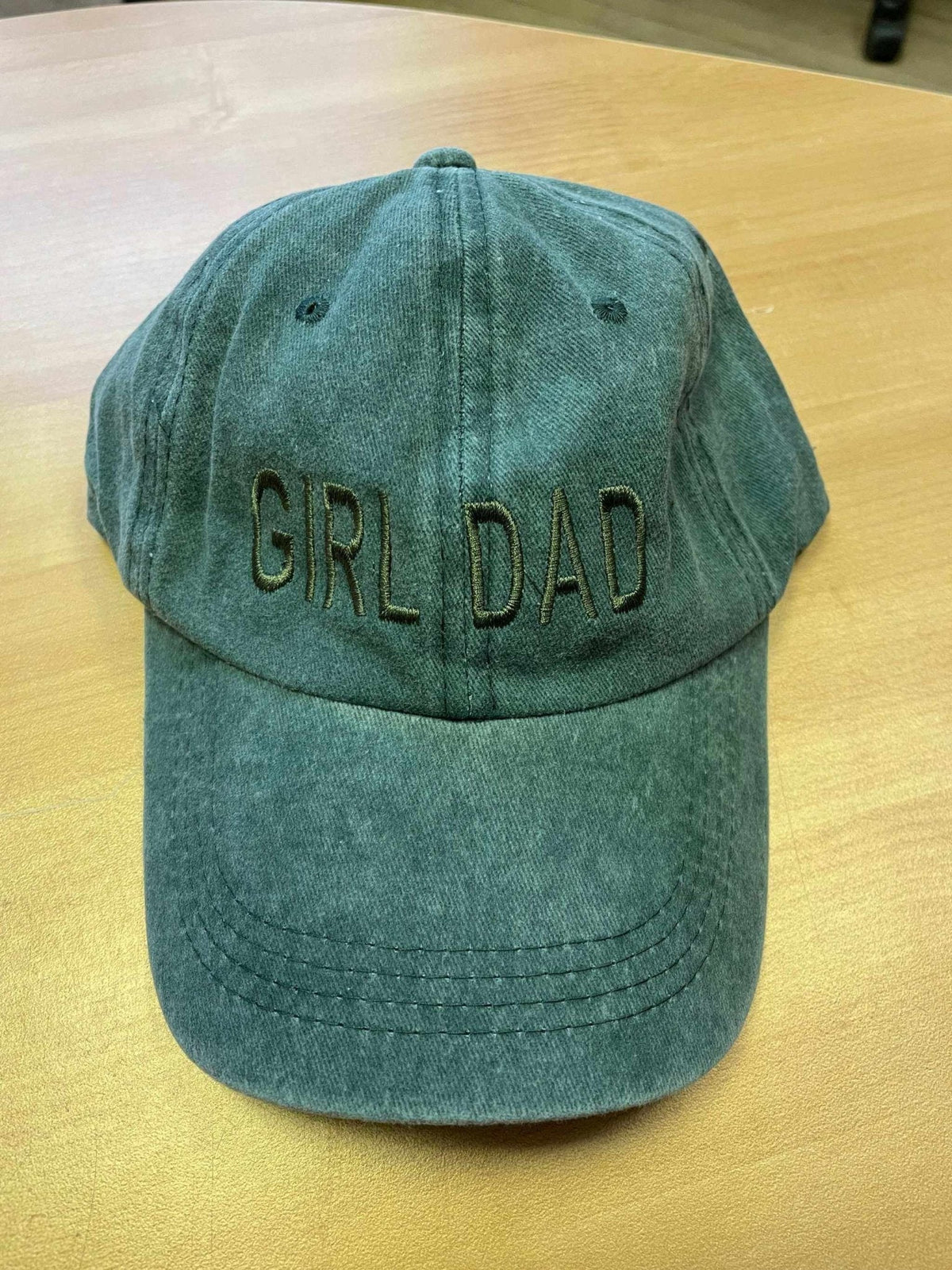 Green "Girl Dad" baseball hat with adjustable strap on wooden surface